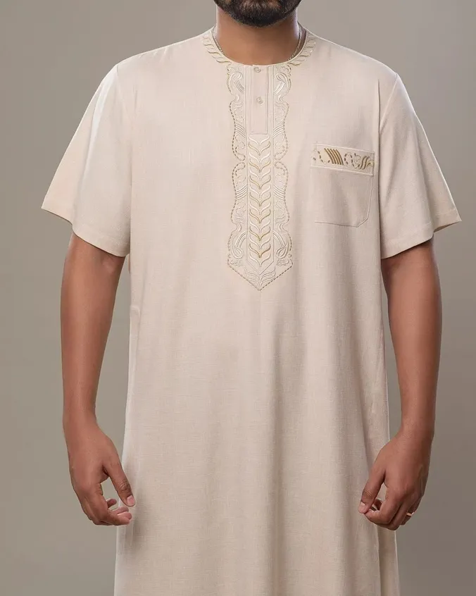 Man wearing a cream short-sleeve thobe with ivory and gold scrollwork embroidery down the neckline and a matching chest pocket
